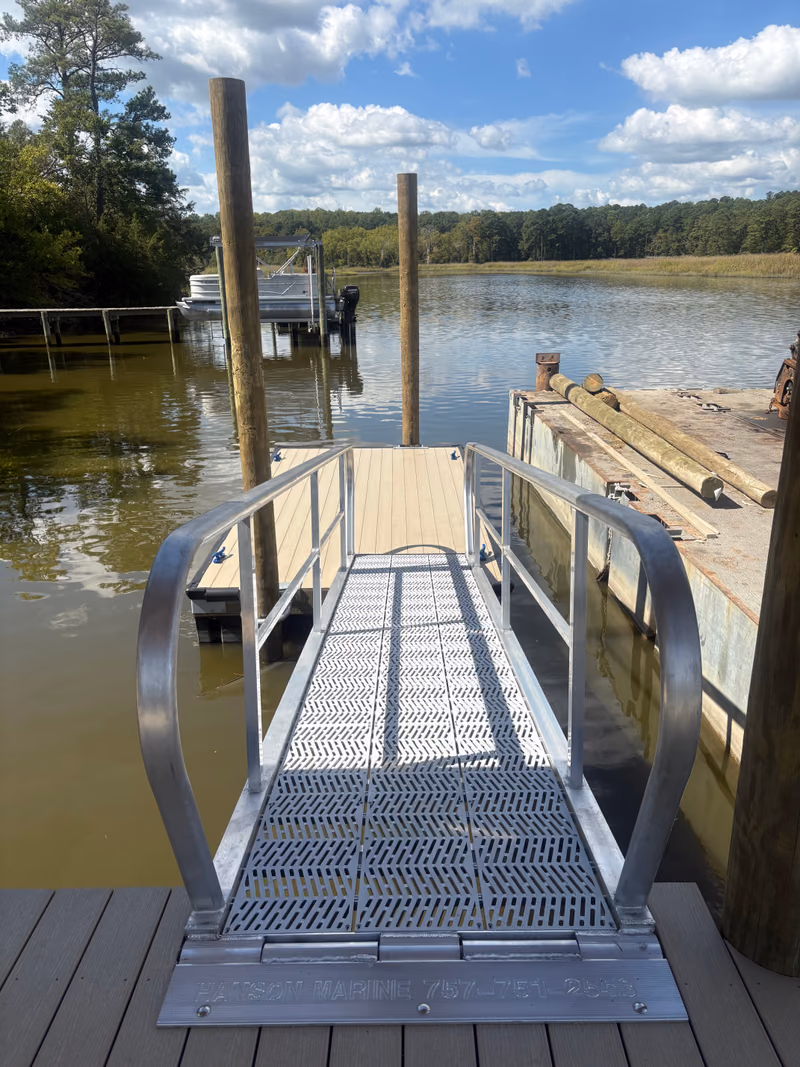 A timber walkway running along a waterfront house with rip rap and marsh beyond.