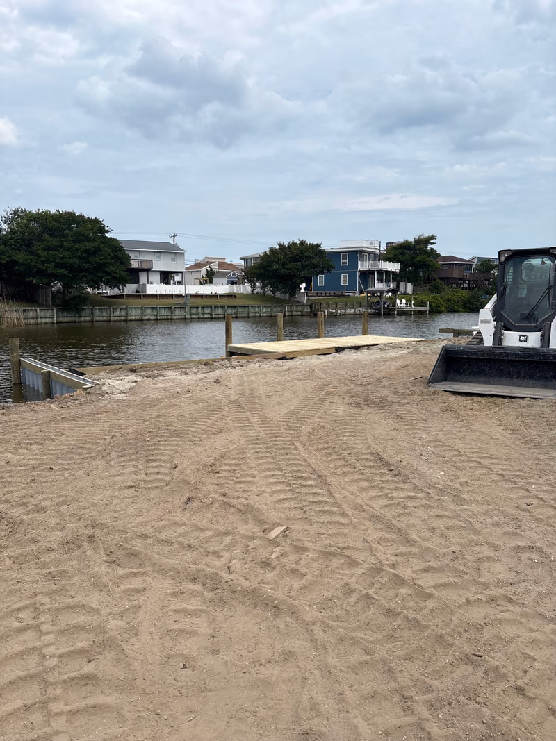 A skid steer grading sand at the water's edge during shoreline work.