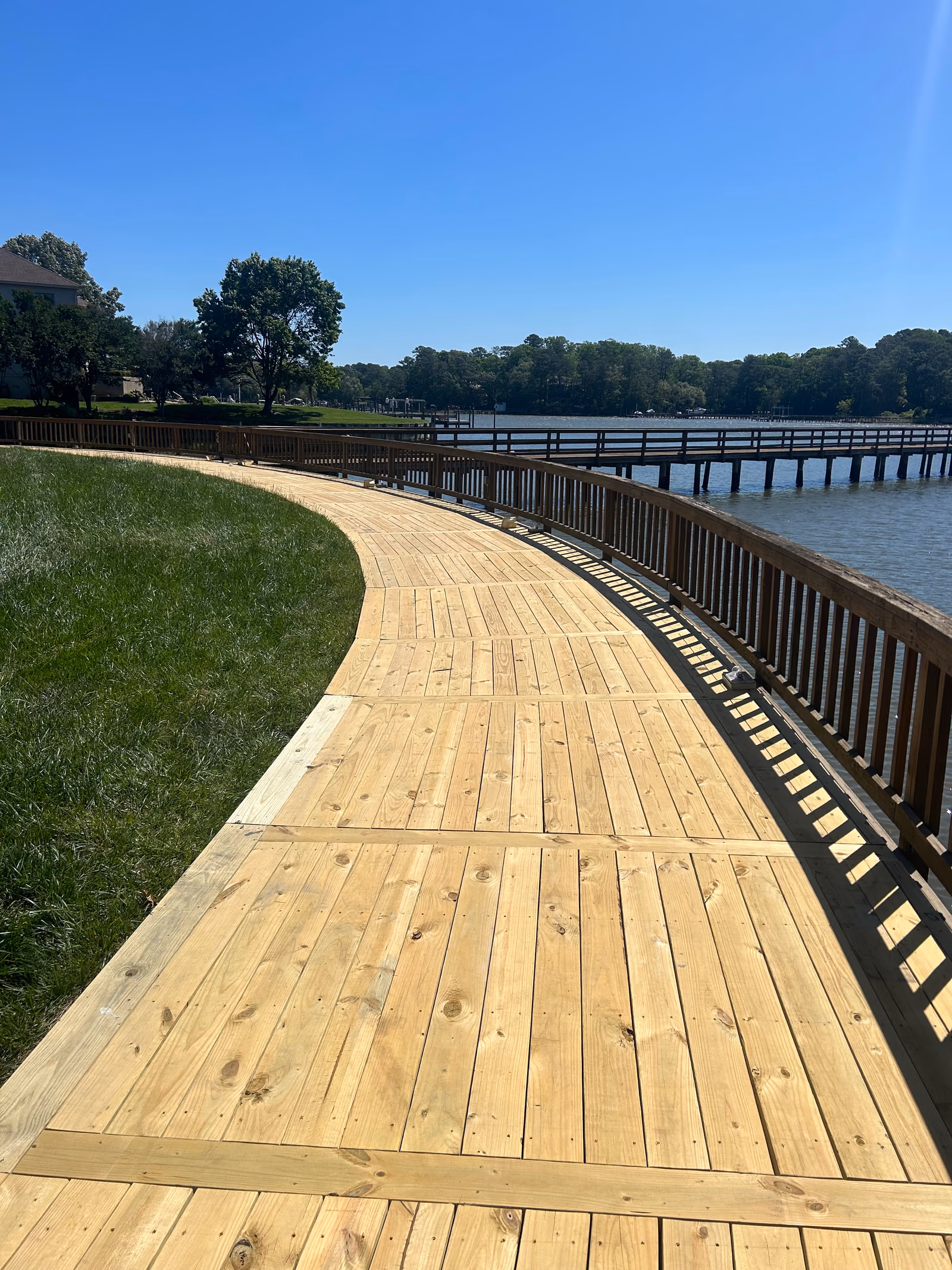 A curving timber boardwalk with a dark railing running along a waterfront lawn.