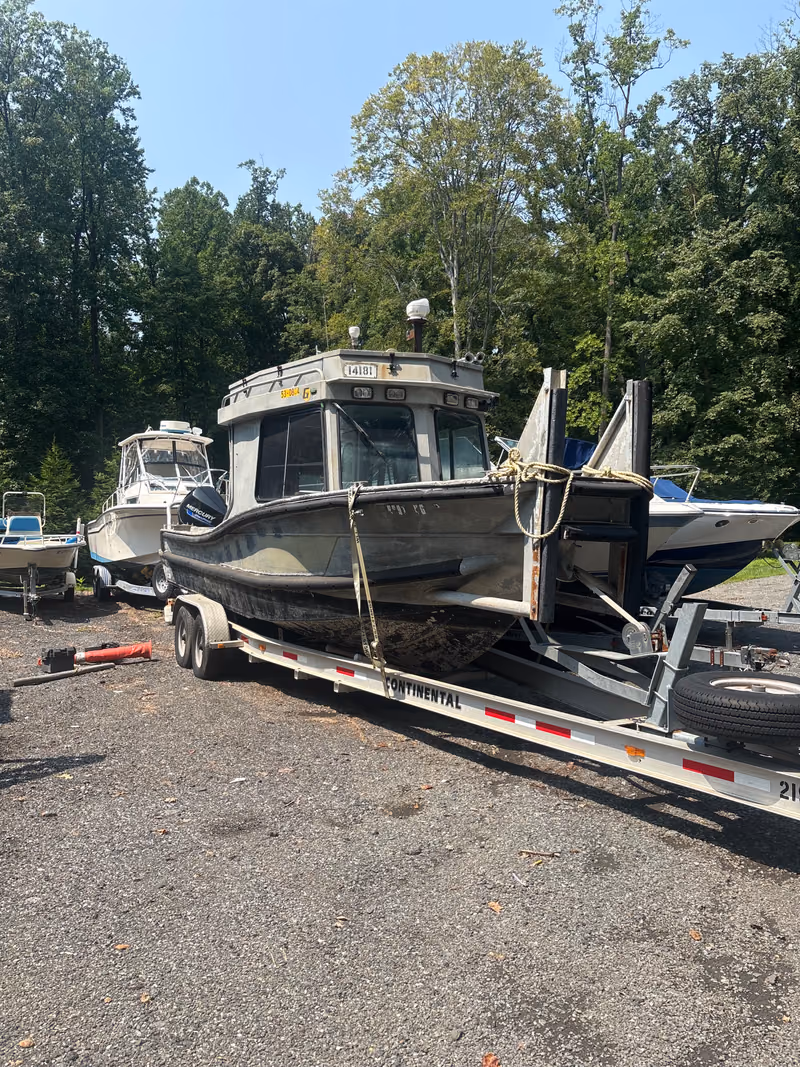 A boat strapped down on its trailer in the yard with others parked behind.