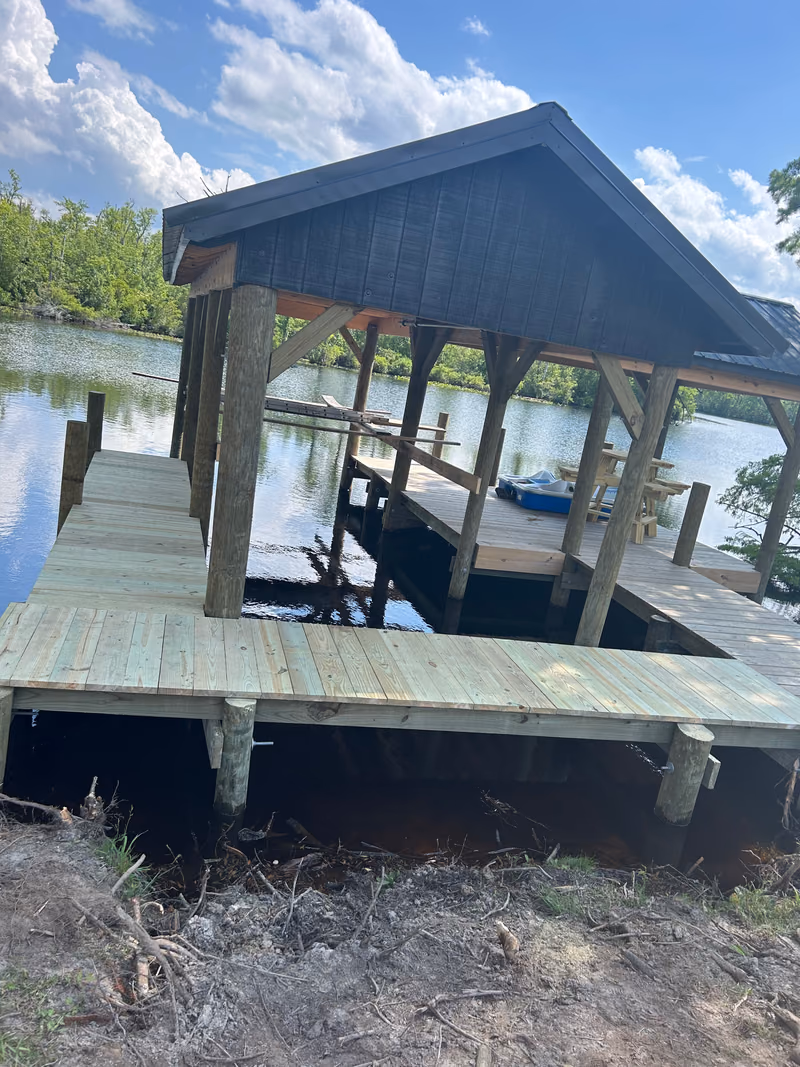 A dark-roofed boathouse over the water on a wooded Currituck creek.