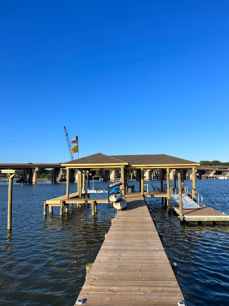 A boathouse and timber dock with a highway bridge crossing behind it.