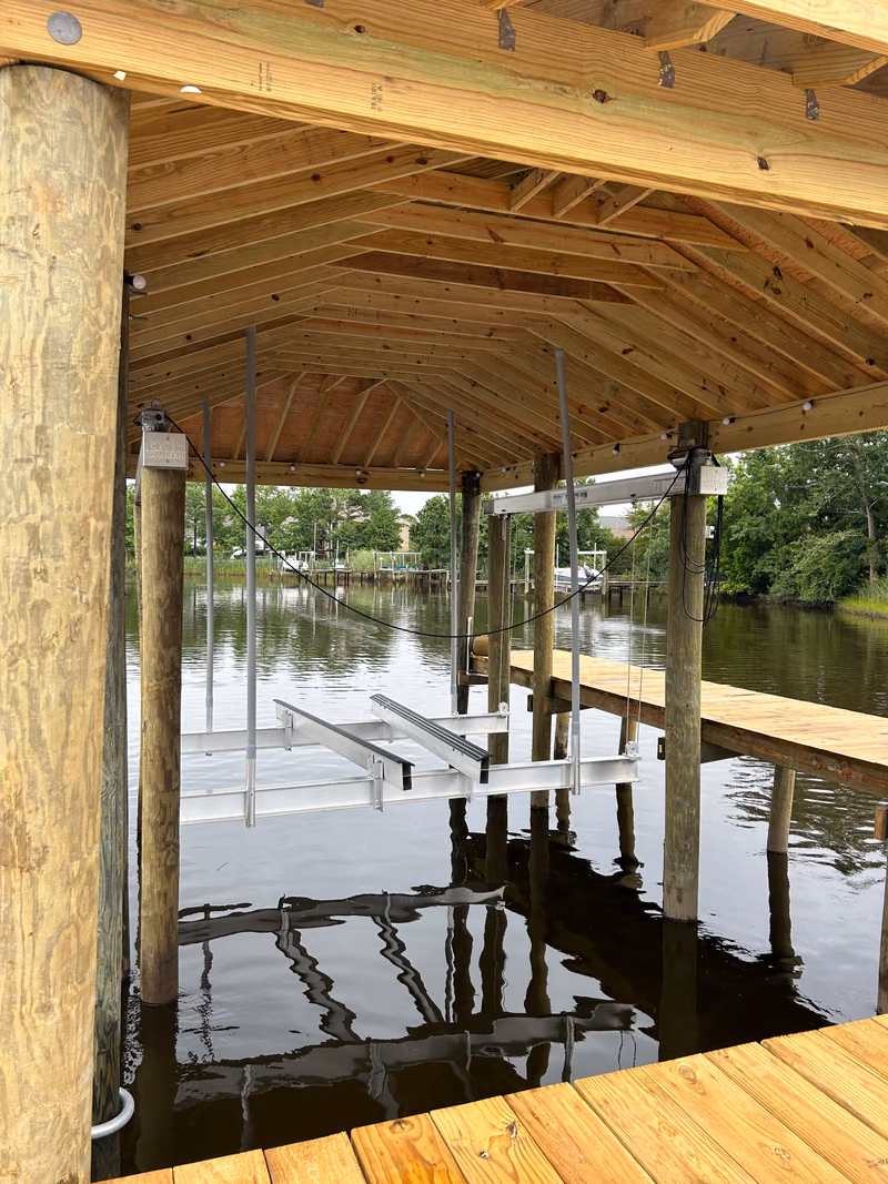 Inside a custom boathouse: exposed rafters overhead, empty boat lift cradle below.