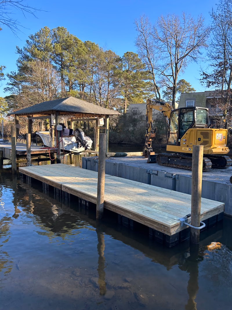 A dock and small boathouse under construction, two excavators working the bank behind.