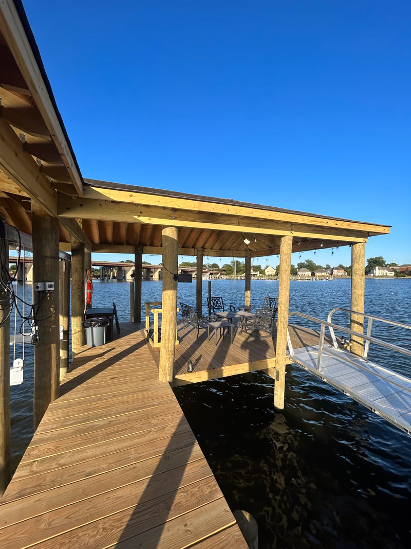 A finished boathouse deck furnished with table and chairs in the shade.