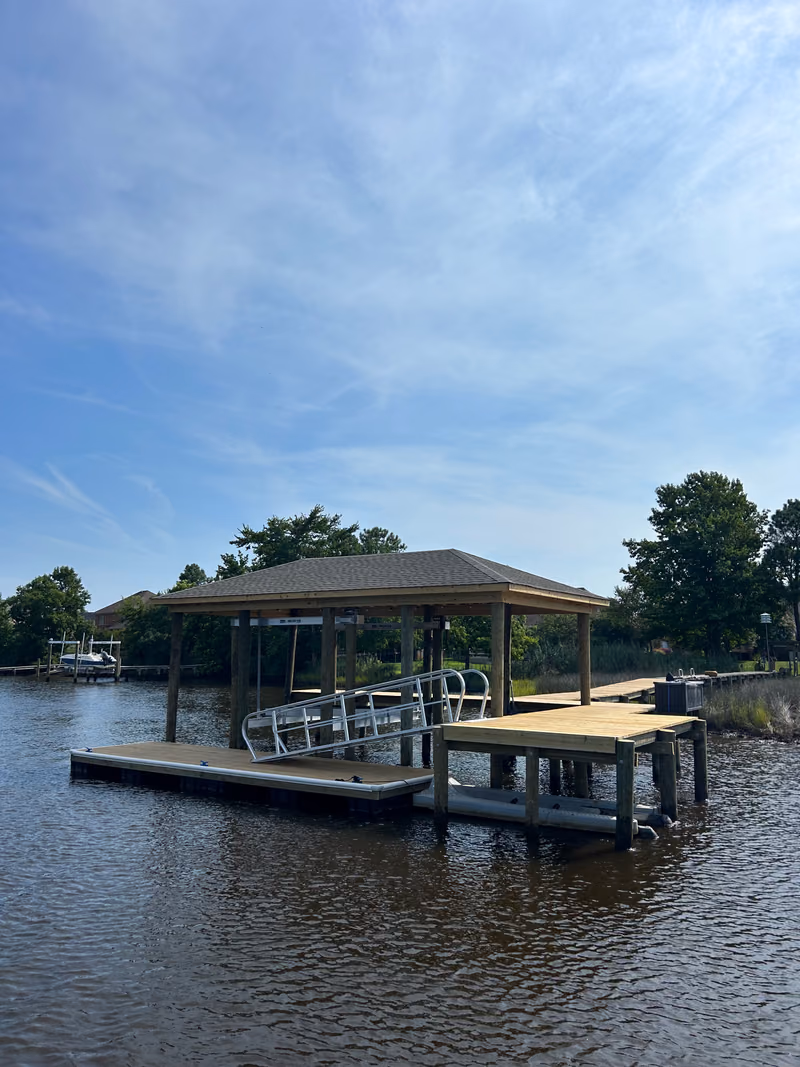 A shingled hip-roof boathouse built over a floating dock and aluminium gangway.