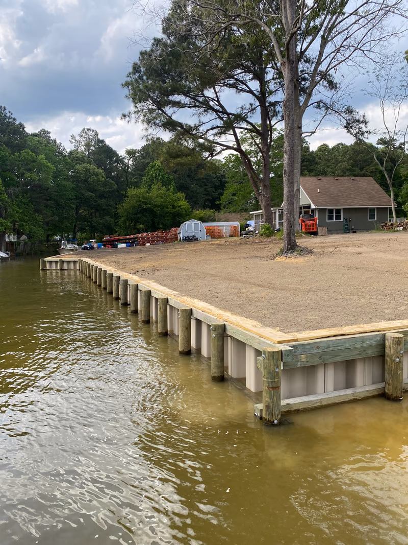 A long shoreline bulkhead wrapping the corner of a lot, fresh sand graded behind.