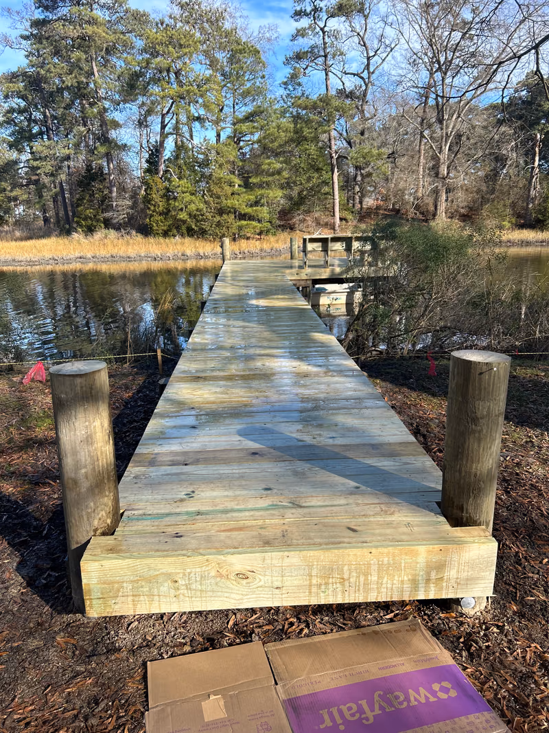 A narrow timber dock walkway crossing a wooded bank down to the water.
