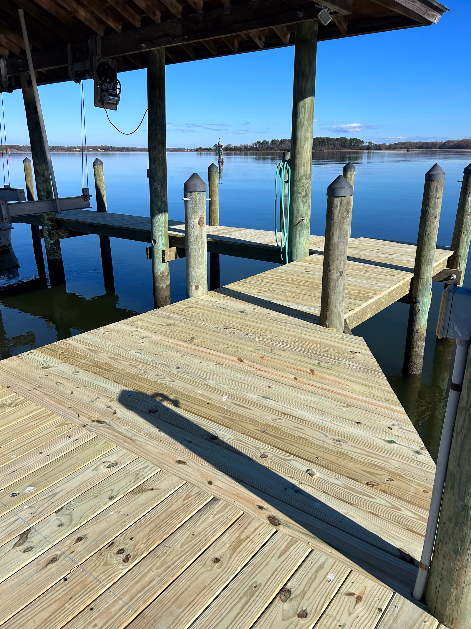 New timber decking inside a covered boat slip, looking out past capped pilings to open water.