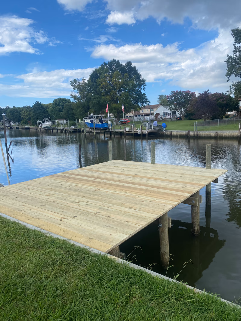 A square timber dock platform off a lawn and seawall on a Hampton Roads creek.