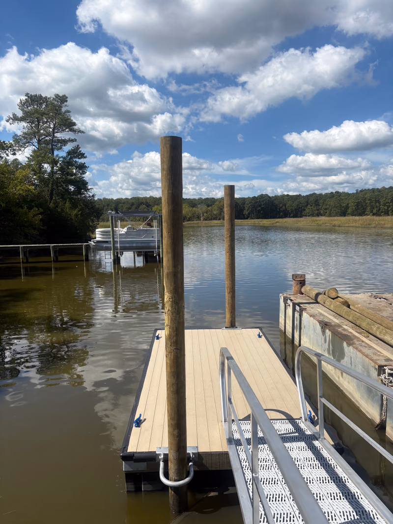 A floating dock with an aluminium gangway and two tall mooring pilings.