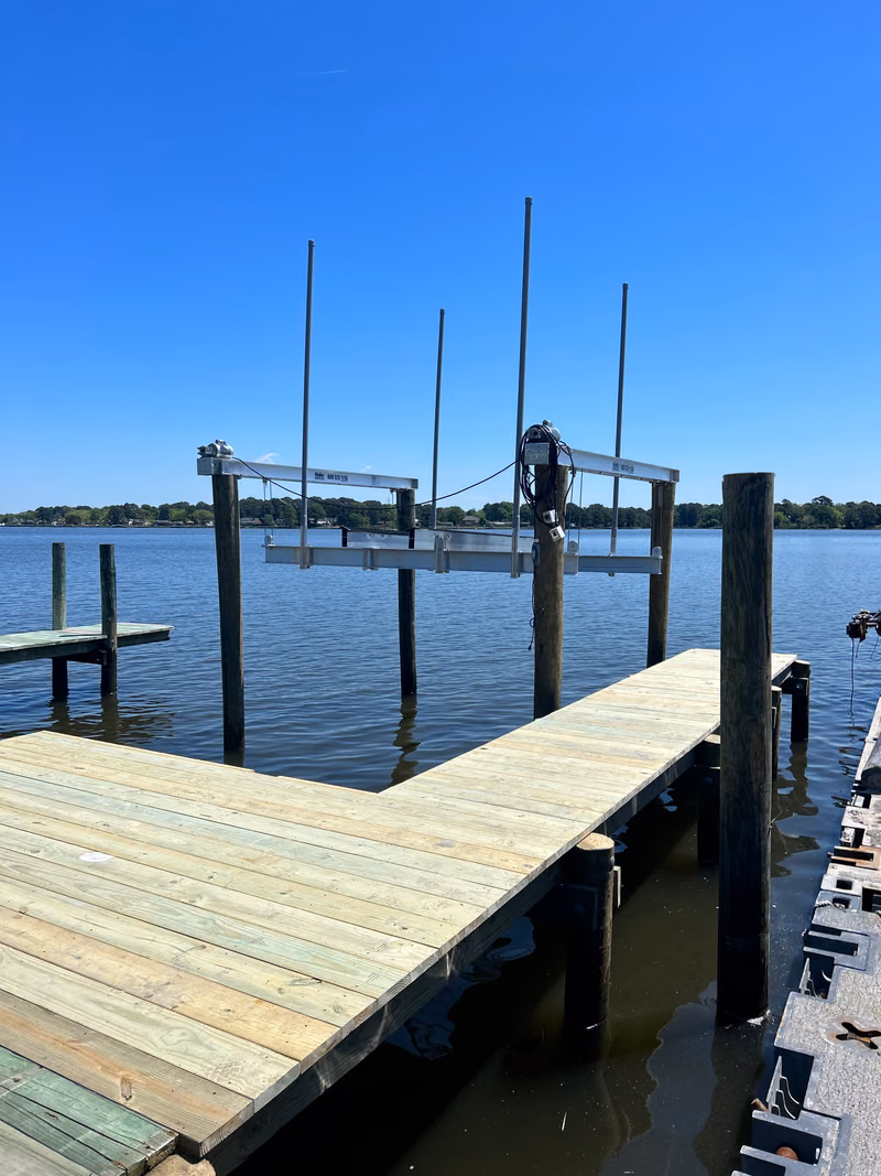 A boat lift frame and motor at the end of a new timber dock on open water.