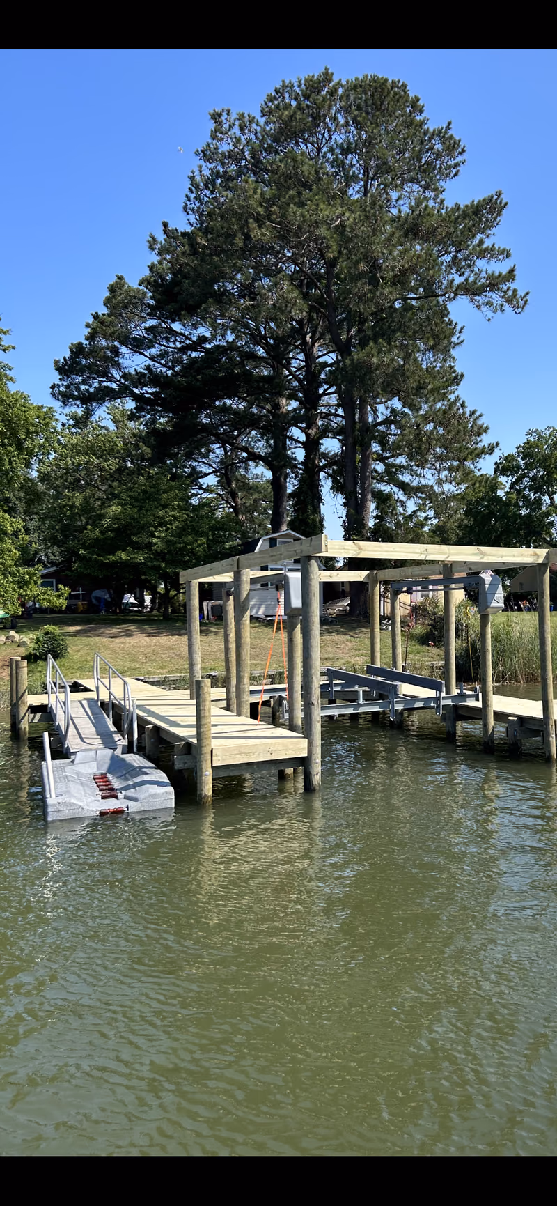 A dock, floating dock and covered boat lift frame under tall pines.