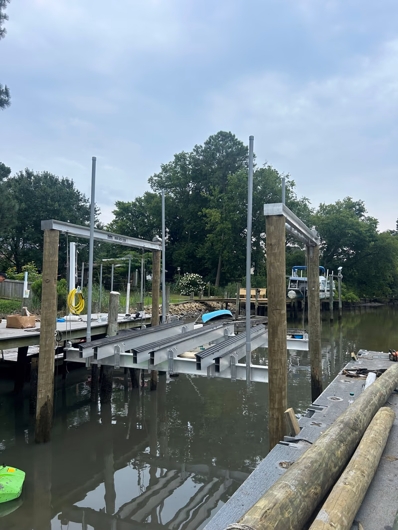 Two boat lift frames on pilings beside a dock, trees along the bank behind.
