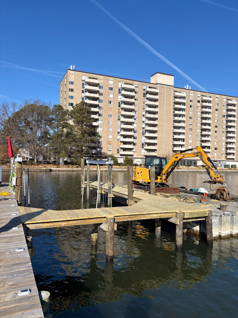 A commercial dock under construction by excavator, high-rise building behind.