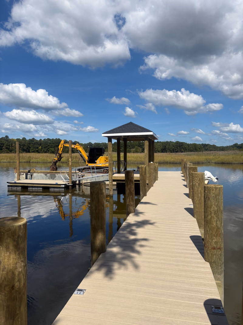 A finished composite pier and roofed gazebo, excavator on the barge alongside.