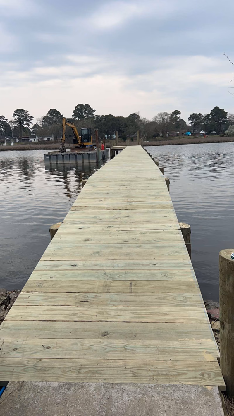 Looking down the length of a newly decked pier, barge and excavator at the far end.