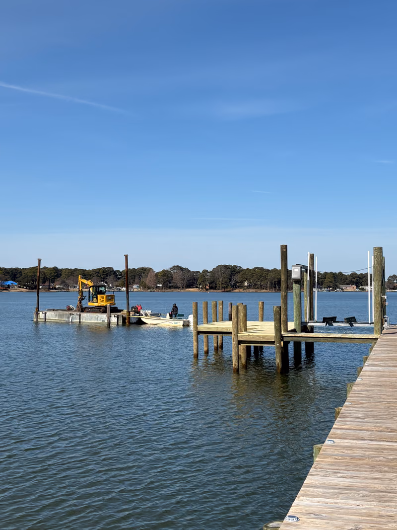 New pier pilings standing in open water with the work barge and crew alongside.