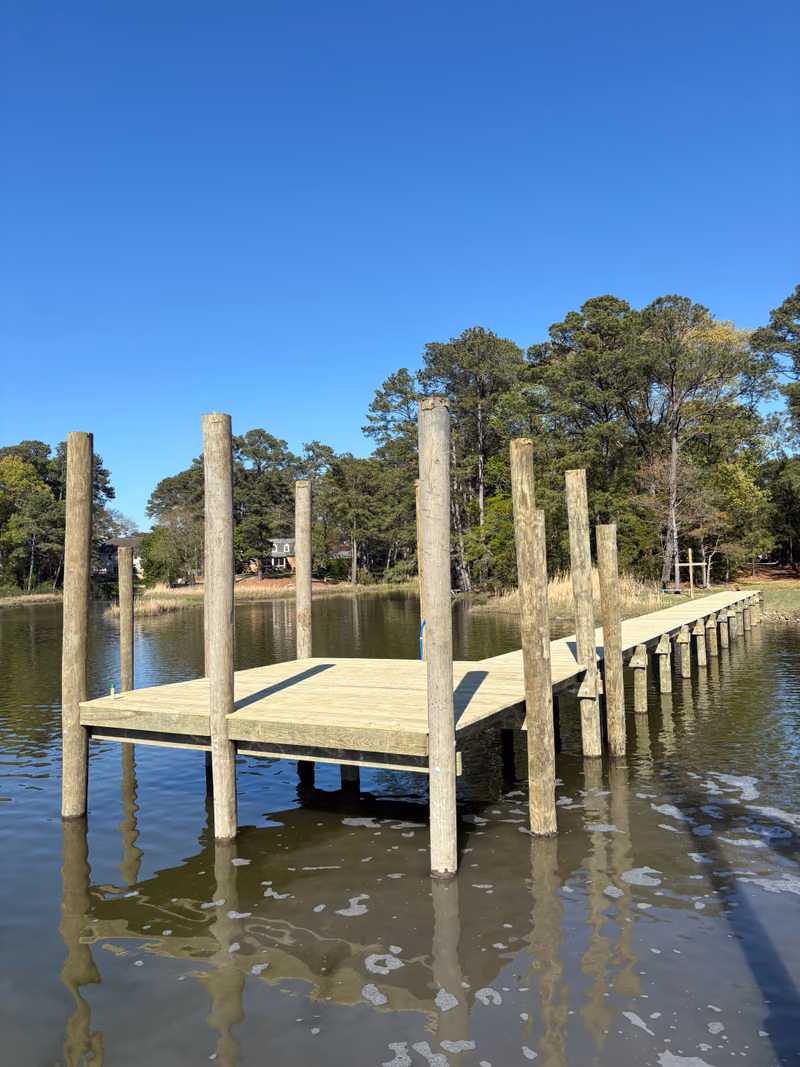 A timber pier platform on tall pilings in a wooded tidal cove.
