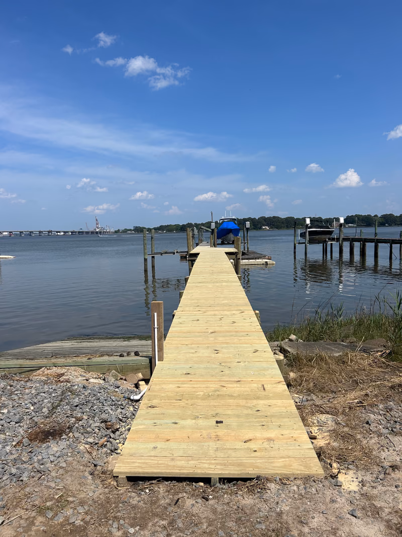A pier running from a gravel bank out to a boat lift, bridge in the distance.
