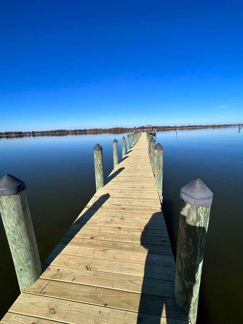 A long timber pier running straight out across flat open water under a clear sky.