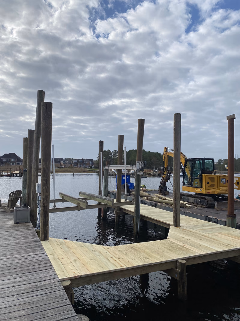 New pilings and part-laid decking for a boat lift, excavator working the bank behind.