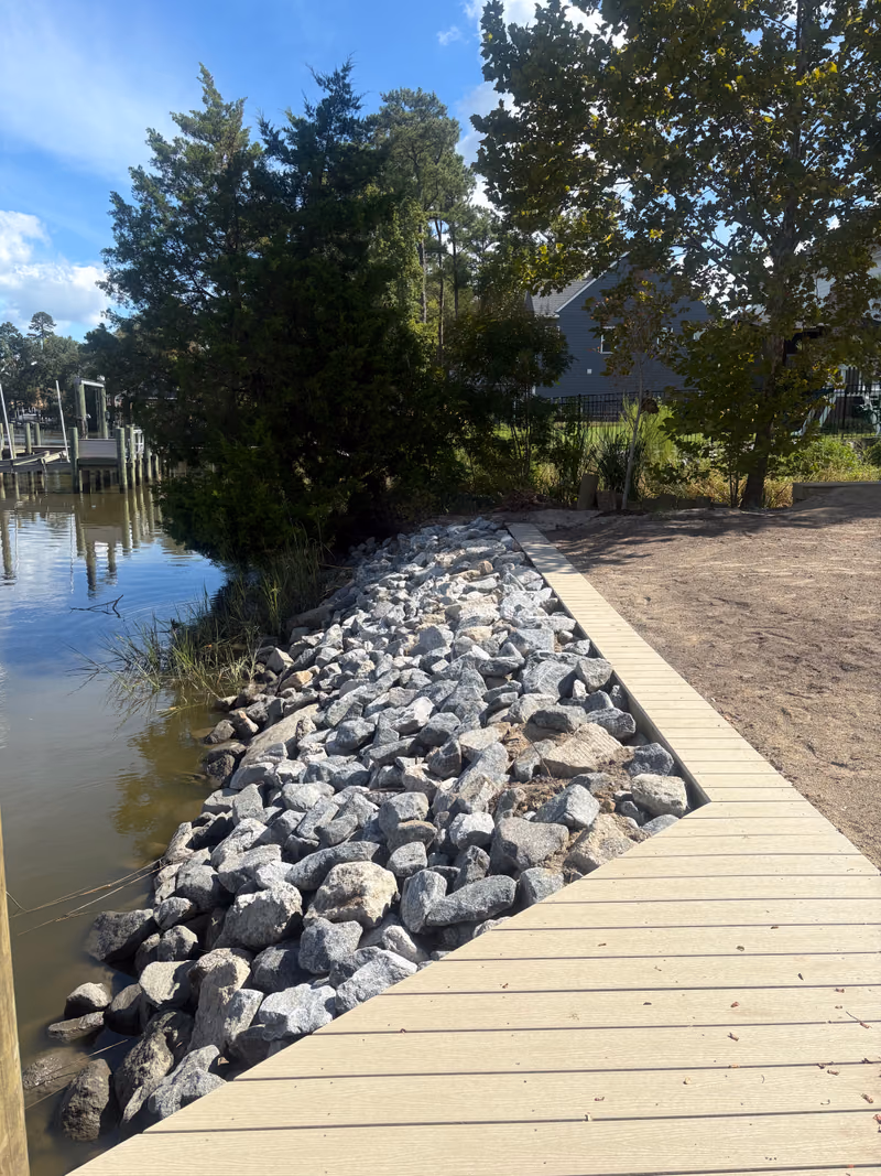 Rip rap armouring a shoreline with a composite walkway and graded sand behind.