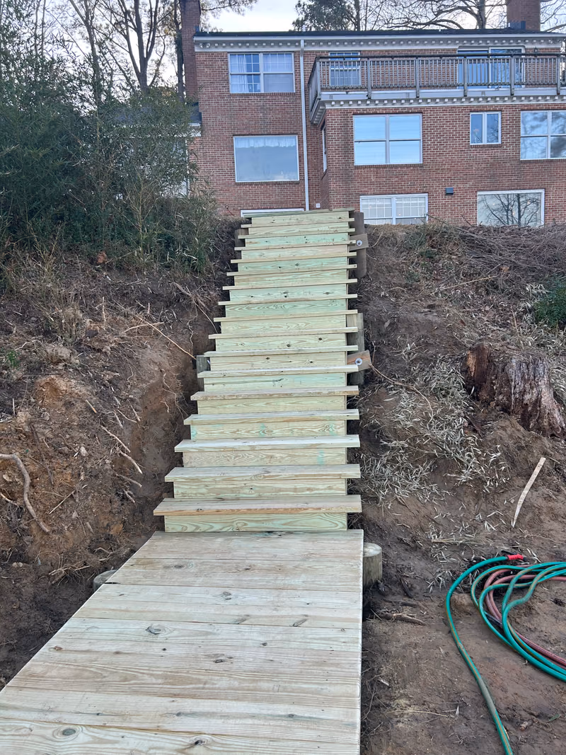 New timber stairs running up a cut bank from a waterfront landing to a brick house.
