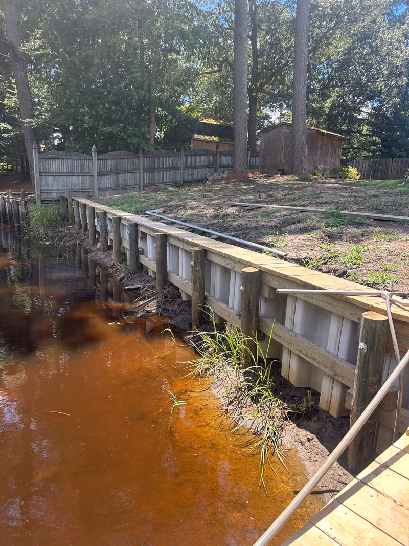 A new vinyl sheet pile bulkhead with a timber cap along a lawn.